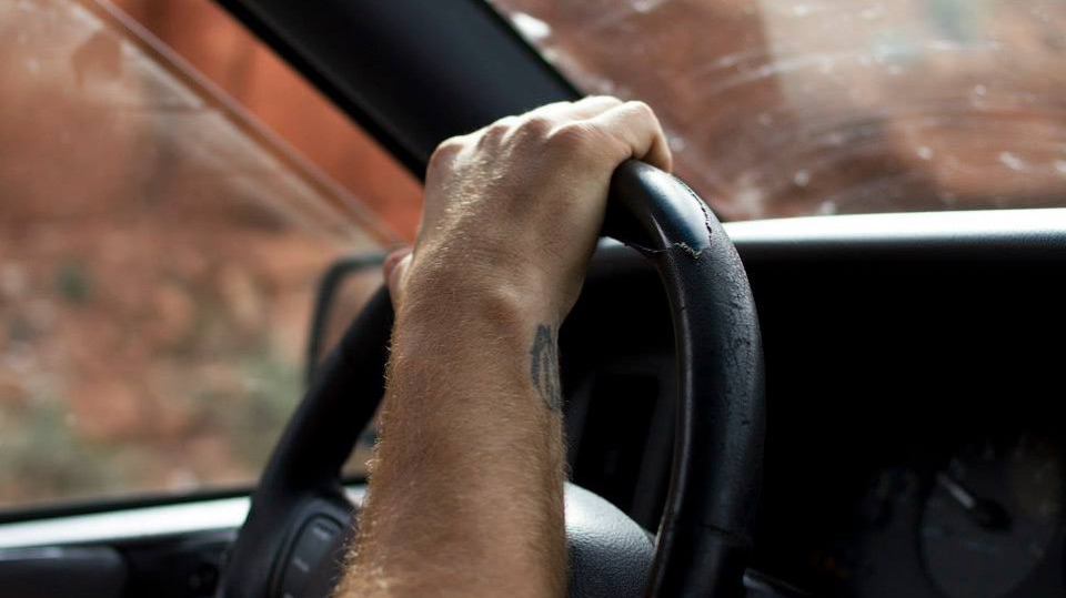 A tattooed hand on the steering wheel of a car driving through red rock country
