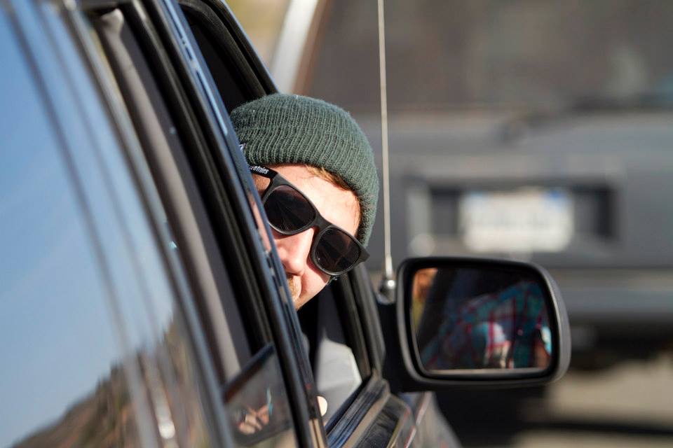 A traveller in a beanie and sunglasses leaning out of a car window
