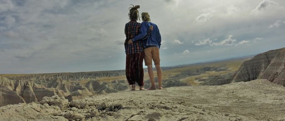 Two travellers, arms around each other, looking out over an eroded badlands landscape