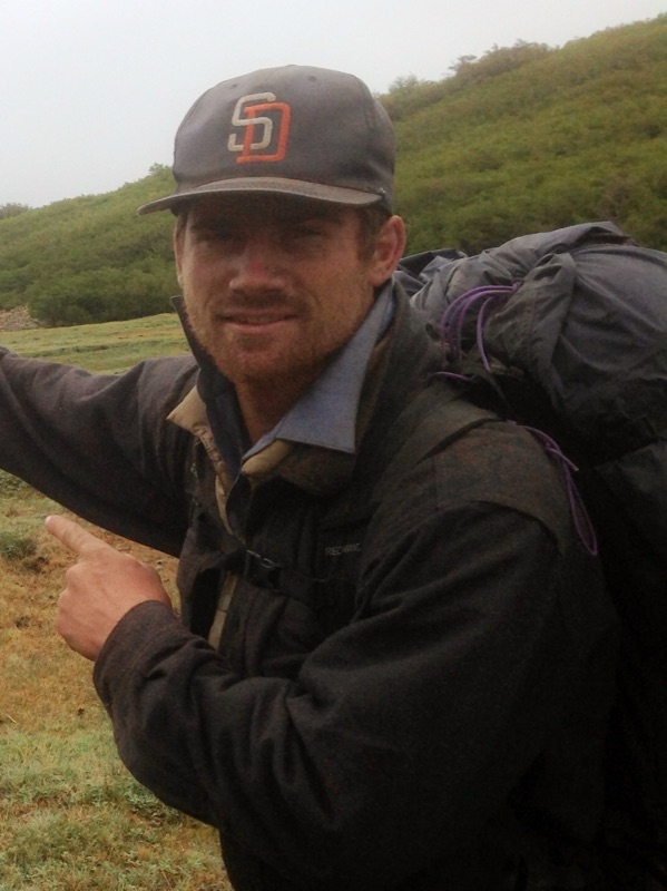 Sonny wearing a San Diego Padres cap and a big backpack on a green hillside